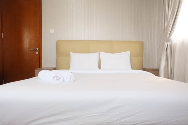 A neatly made bed with white linens and pillows, a wooden door, and a light-colored headboard. - Comfy 2Bedroom At Signature Park Grande Apartment (Jakarta)
