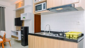 A modern kitchen with a built-in microwave, stove, and sink. There is a wooden cabinet and a small shelf with a plant. - Warm And Cozy 2Br Signature Park Grande Apartment (Jakarta)