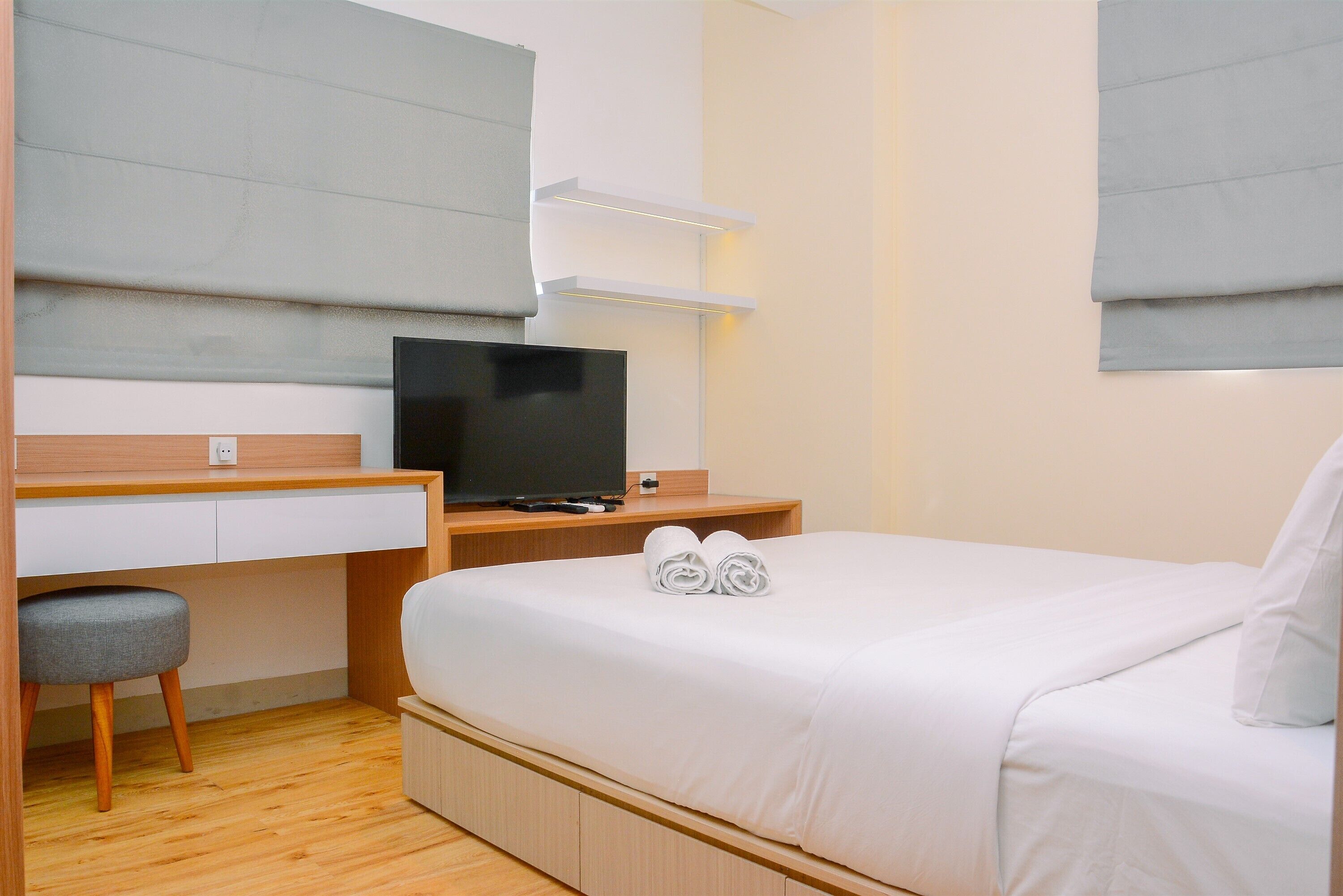 A hotel room with a bed, a desk with a television, a chair, and a window with blinds.
