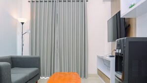 A modern living room with a grey sofa, an orange ottoman, a flat-screen TV, and a water dispenser. - Warm And Cozy 2Br Signature Park Grande Apartment (Jakarta)