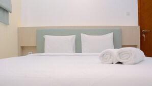 A neatly made bed with white linens and pillows, a rolled towel on the side, and a wooden headboard. - Warm And Cozy 2Br Signature Park Grande Apartment (Jakarta)