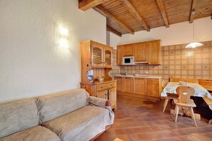 A cozy kitchen with wooden cabinets, a microwave, a dining table with chairs, and a sofa.