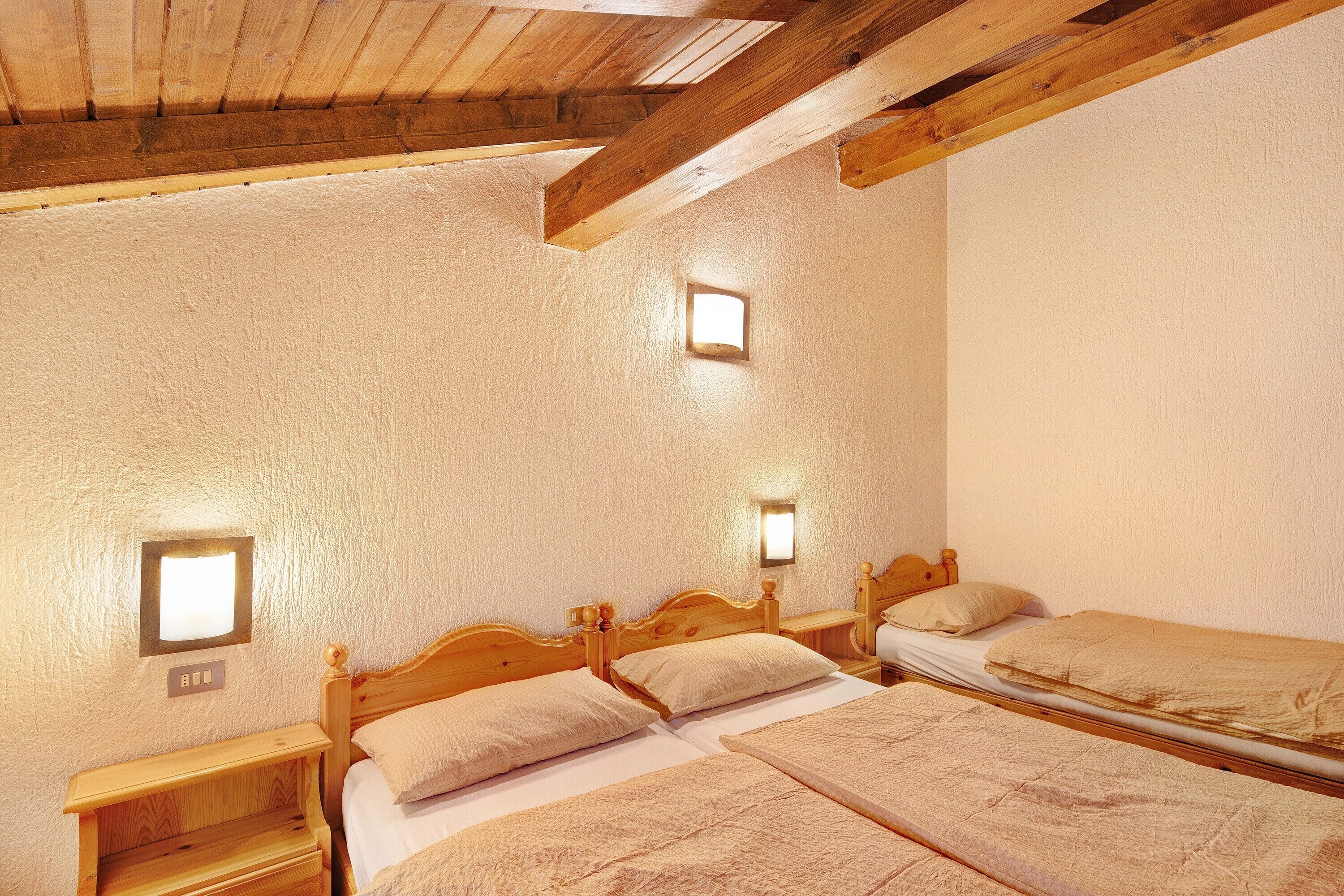 A room with three wooden beds, a small window, and a wooden ceiling.