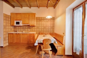 A compact kitchen with wooden cabinets, a microwave, a dining table with a bench, and a hanging light fixture.