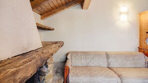 Ein Zimmer mit Kamin aus Stein, Holzbalken, einer Couch und einer Holztür.