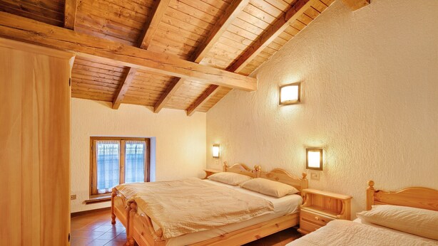 Ein Schlafzimmer mit zwei hölzernen Betten, einem Nachttisch aus Holz, einem Fenster mit Vorhängen und einer Holzbalkendecke.