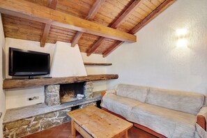 A cozy room with a stone fireplace, wooden ceiling beams, a flat-screen TV, and a beige sofa.