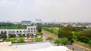 Vista de um horizonte urbano com um edifício em destaque, com janelas em arco e telhado plano, cercado por áreas verdes e uma estrada.