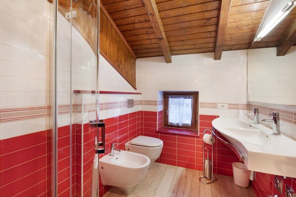 Een badkamer met rode en witte tegels, een houten plafond, een raam, een wastafel en een douchetoilet.