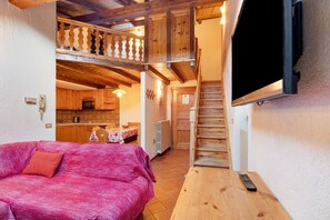 Ein gemütliches Zimmer mit einem Bett, einem Holztisch, einem an der Wand montierten Fernseher und einer Treppe, die in einen oberen Bereich führt.