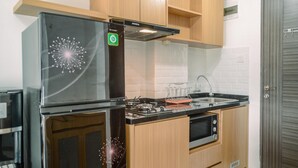 A modern kitchen with a black refrigerator, a stove, and wooden cabinets. - Stunning And Comfy Studio Amazana Serpong Apartment (South Tangerang)