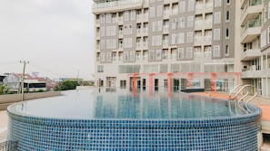 Un edificio moderno con una piscina en la azotea, que cuenta con un borde de azulejos azules y brillantes y una barandilla de seguridad roja.