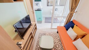 A compact hotel room with a television, a small table, a sofa with cushions, and a patterned rug. - Cozy And Spacious 1Br Apartment At Parkland Avenue (South Tangerang)