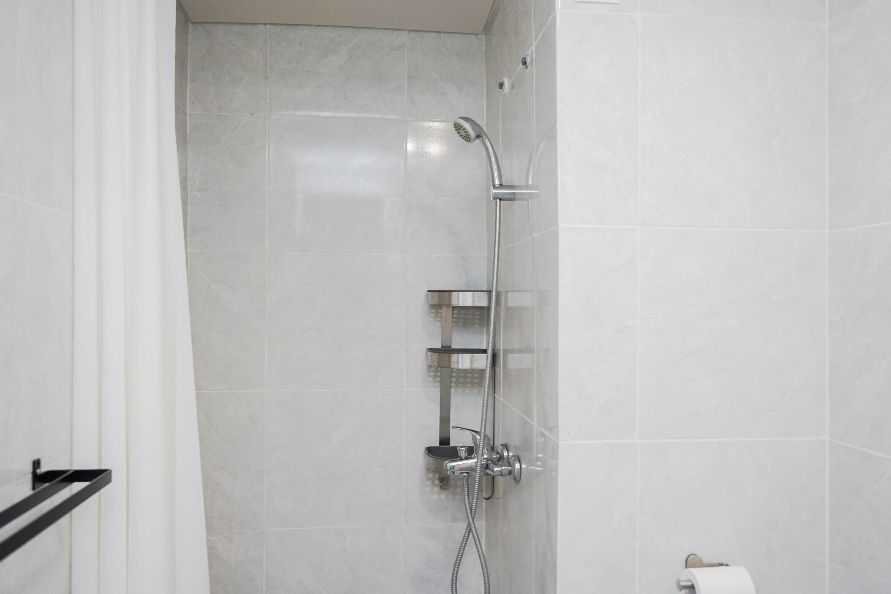 A modern bathroom with a shower, tiled walls, and a toilet paper holder.