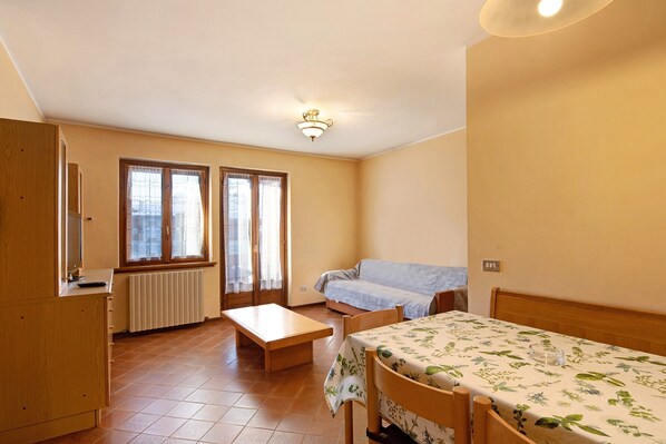 A small, well-lit room with a bed, a table, a bench, and a radiator.
