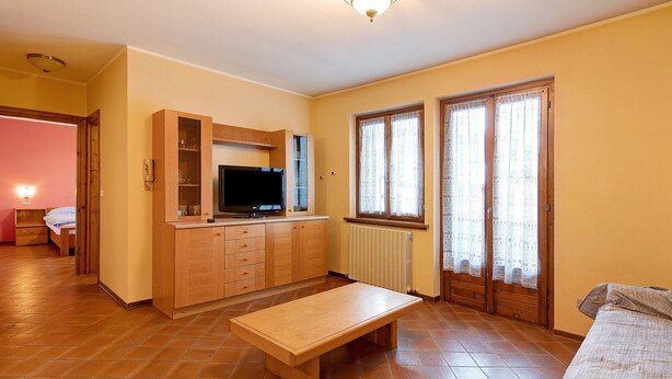 A room with a wooden bench, a television, a cabinet, and a window with curtains. - Apartment 'Chalet Meridiana 8' with Mountain View (Livigno)