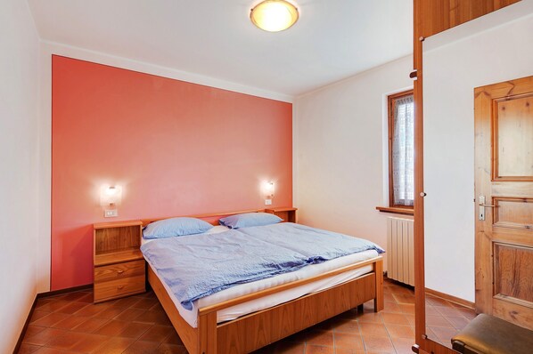 Une chambre à coucher avec un lit en bois, deux tables de chevet, une fenêtre avec des rideaux et un radiateur.