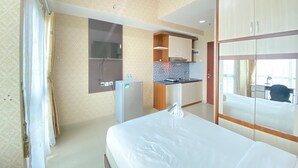 A hotel room with a bed, a small kitchenette, a mirror, and a sliding door. - Modern Studio Room At Taman Melati Jatinangor Apartment (Hegarmanah)