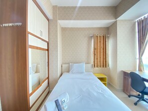 A hotel room with a bed, a desk, a chair, a wardrobe, and a curtain. - Modern Studio Room At Taman Melati Jatinangor Apartment (Hegarmanah)