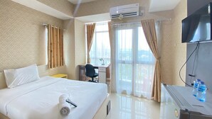 A hotel room with a bed, a desk, a chair, an air conditioner, a TV, and a window with curtains. - Modern Studio Room At Taman Melati Jatinangor Apartment (Hegarmanah)
