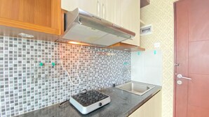 A kitchen with a tiled backsplash, a built-in stove, a sink, and wooden cabinets. - Modern Studio Room At Taman Melati Jatinangor Apartment (Hegarmanah)