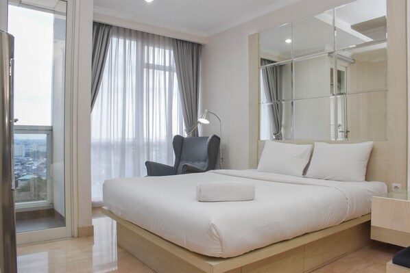 A modern hotel room with a large bed, a chair, a desk, and a large window with curtains.