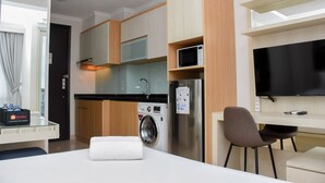 A compact hotel room with a kitchenette, a washing machine, a flat-screen TV, and a small seating area. - Comfortable And Warm Studio Room At Menteng Park Apartment (Jakarta)