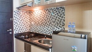 A kitchen with a black countertop, a stainless steel sink, and a refrigerator. There are two water bottles on top of the refrigerator. - Warm Studio Apartment At Tamansari Papilio (Surabaya)