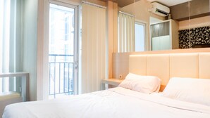 A hotel room with a large bed, a bedside table, a mirror, and a view of the outside. - Warm Studio Apartment At Tamansari Papilio (Surabaya)