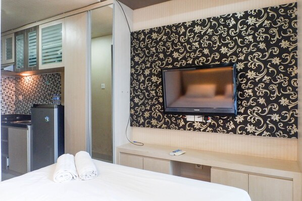 A hotel room with a bed, a TV mounted on the wall, a small desk, and a kitchenette area.