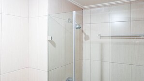 A glass-enclosed shower with a handheld showerhead, tiled walls, and a towel rack. - Warm Studio Apartment At Tamansari Papilio (Surabaya)