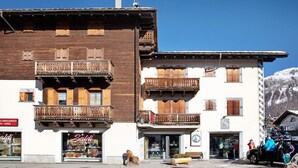 Un bâtiment doté de balcons en bois, un magasin avec une enseigne, et une montagne en arrière-plan.