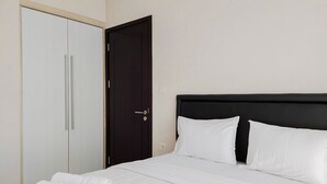 Un lit bien fait, avec du linge de lit blanc et des oreillers, une tête de lit sombre et une armoire fermée dotée de poignées argentées.