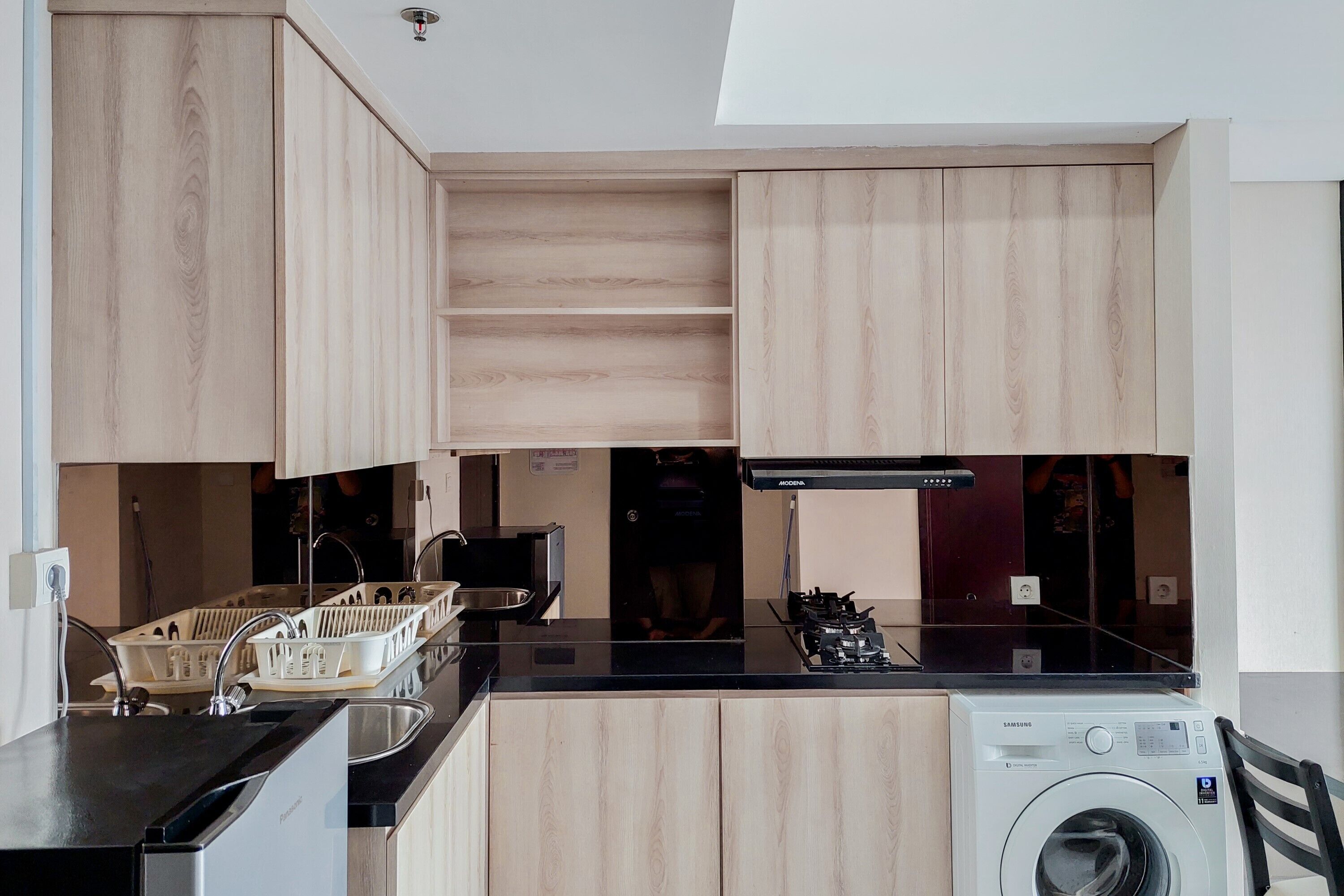 A compact kitchen with wooden cabinets, a black countertop, a washing machine, and a microwave.