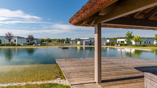 Ein modernes Gebäude mit Pool, einer Holzterrasse und einem überdachten Bereich mit einem Reetdach.