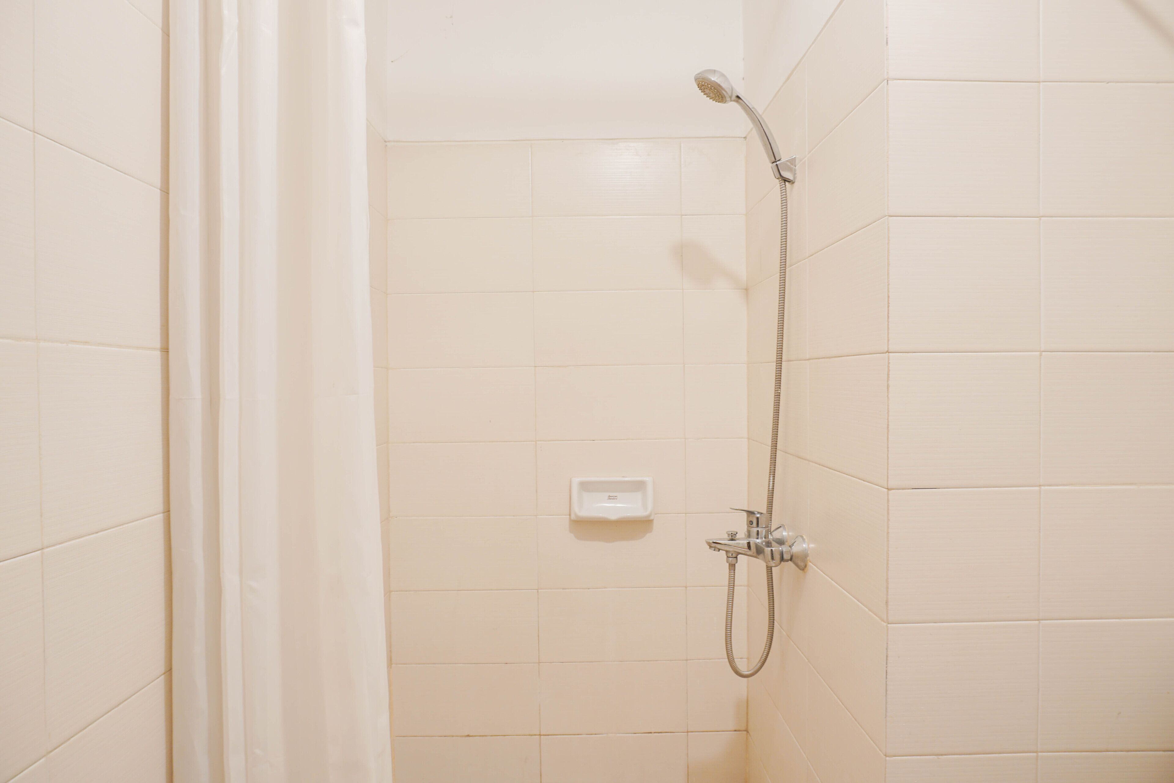 A shower area with a handheld showerhead and a wall-mounted control panel.