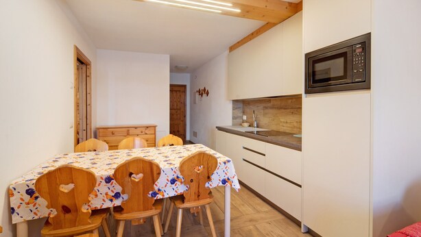 Une cuisine équipée d’un four à micro-ondes, de placards en bois, d’une table recouverte d’une nappe à motifs floraux et de chaises en bois.