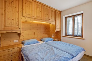 A wooden bedroom with two beds, a window, and built-in cabinets.