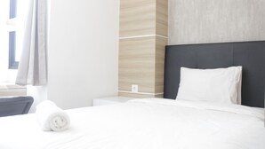 Una camera d'albergo con un letto rifatto, una testiera scura e una parete di colore chiaro con motivo effetto legno.