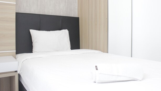 Un letto rifatto con lenzuola bianche e una testiera nera in una stanza moderna con pannelli in legno chiaro e un armadio bianco.