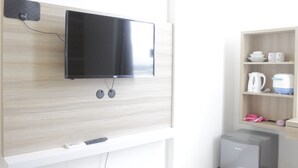 Una camera moderna con TV a schermo piatto a parete, un piccolo frigorifero e uno scaffale con oggetti da cucina.