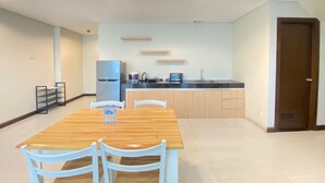 Eine moderne Küche mit Kühlschrank, Herd und Spüle. Ein Essbereich mit Holztisch und weißen Stühlen ist ebenfalls vorhanden.