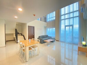 A spacious living area with a dining table, sofa, and large windows. - Fabulous 2Br Loft Apartment With Private Bathub At El Royale (Bandung)