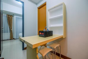 A room with a wooden desk, two chairs, a minibar, and a door with curtains. - Nice And Elegant 1Br At Royal Heights Apartment (Bogor)