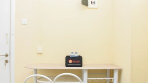 Une petite pièce avec une porte blanche, un mur beige, une table blanche sur laquelle se trouve un sac noir portant l’inscription « travelio », et deux chaises blanches.