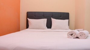 Un lit bien fait, avec une tête de lit noire, du linge de lit blanc et deux serviettes enroulées posées sur le côté.