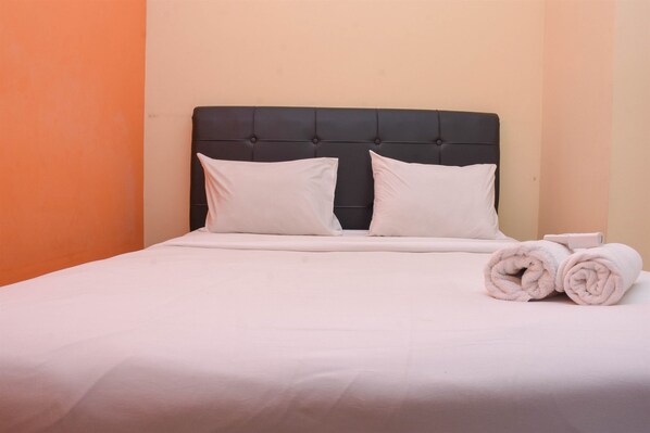 A neatly made bed with a black headboard, white bedding, and two rolled towels on the side.