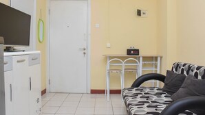 Un espace de vie compact comprenant un canapé, un téléviseur, un lave-linge et une petite table avec des chaises.