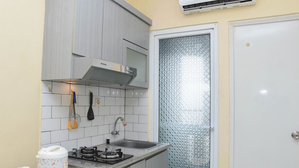Une cuisine compacte équipée d’une cuisinière à gaz, d’un four à micro-ondes et d’un évier. On y trouve une petite table avec une bouilloire et une multiprise. Les murs sont recouverts de carreaux, et il y a une porte en verre dépoli.