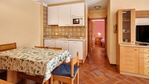 Eine kompakte Küche mit Mikrowelle, Holzschränken, einem Esstisch mit Stühlen und einem Fernseher auf einem Holzschrank.